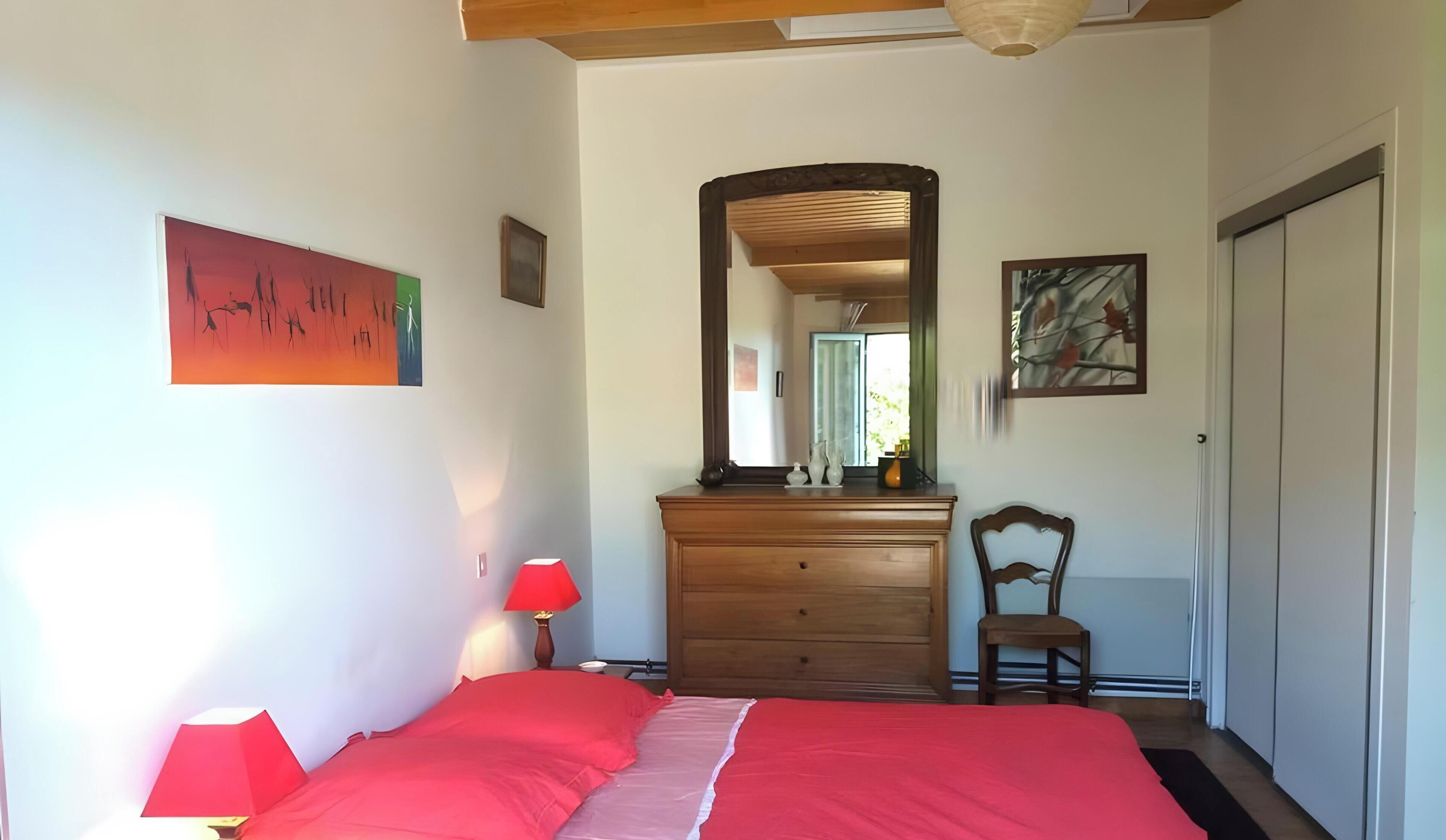 A bedroom with a bed, dresser, chair, and artwork on the walls.