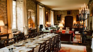 Une salle à manger avec une longue table dressée pour le repas, des murs en pierre et un lustre.