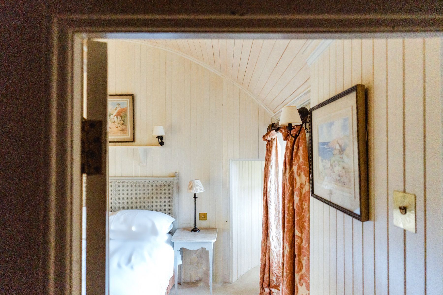 A room with a bed, a small table, a lamp, and a framed picture on the wall.