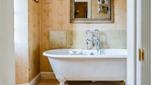 Une baignoire classique sur pieds, dotée d’un robinet moderne, d’un petit porte-savon et d’un miroir placé au-dessus.