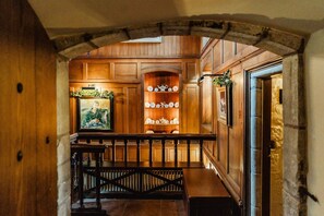 A wooden interior with a bench, a shelf with decorative items, and a framed picture.