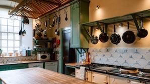 A kitchen with a wooden countertop, a stove, hanging pots, and a window.