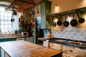 A kitchen with a wooden countertop, a stove, hanging pots, and a window.