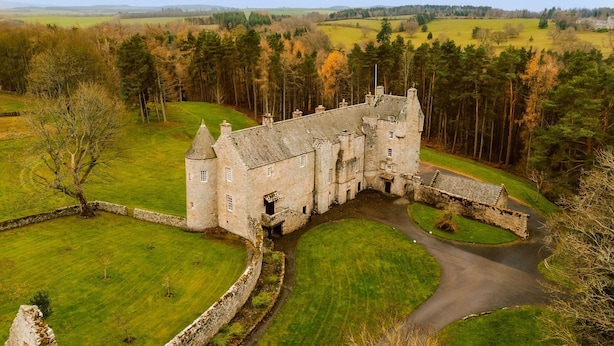 Un château doté d’un fossé, entouré d’un paysage verdoyant et d’arbres.