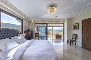 A spacious bedroom with a large bed, a chandelier, and a balcony with a view. - Villa Verity - Nine Bedroom Villa, Sleeps 21 (Porto Germeno)