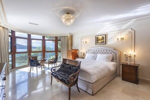 A spacious bedroom with a large bed, a chandelier, a painting, and a view of the outdoors.