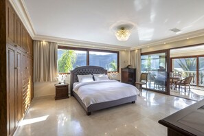 A spacious bedroom with a large bed, a nightstand, a dresser, and a balcony with outdoor furniture.