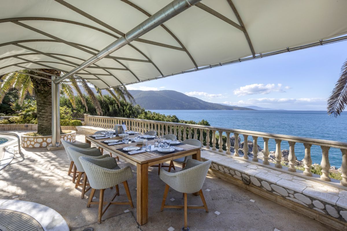 An outdoor dining area with a table set for four, overlooking a body of water and mountains.