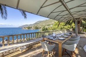 Un área de comedor al aire libre con una mesa preparada para cuatro, con vista a un paisaje costero.