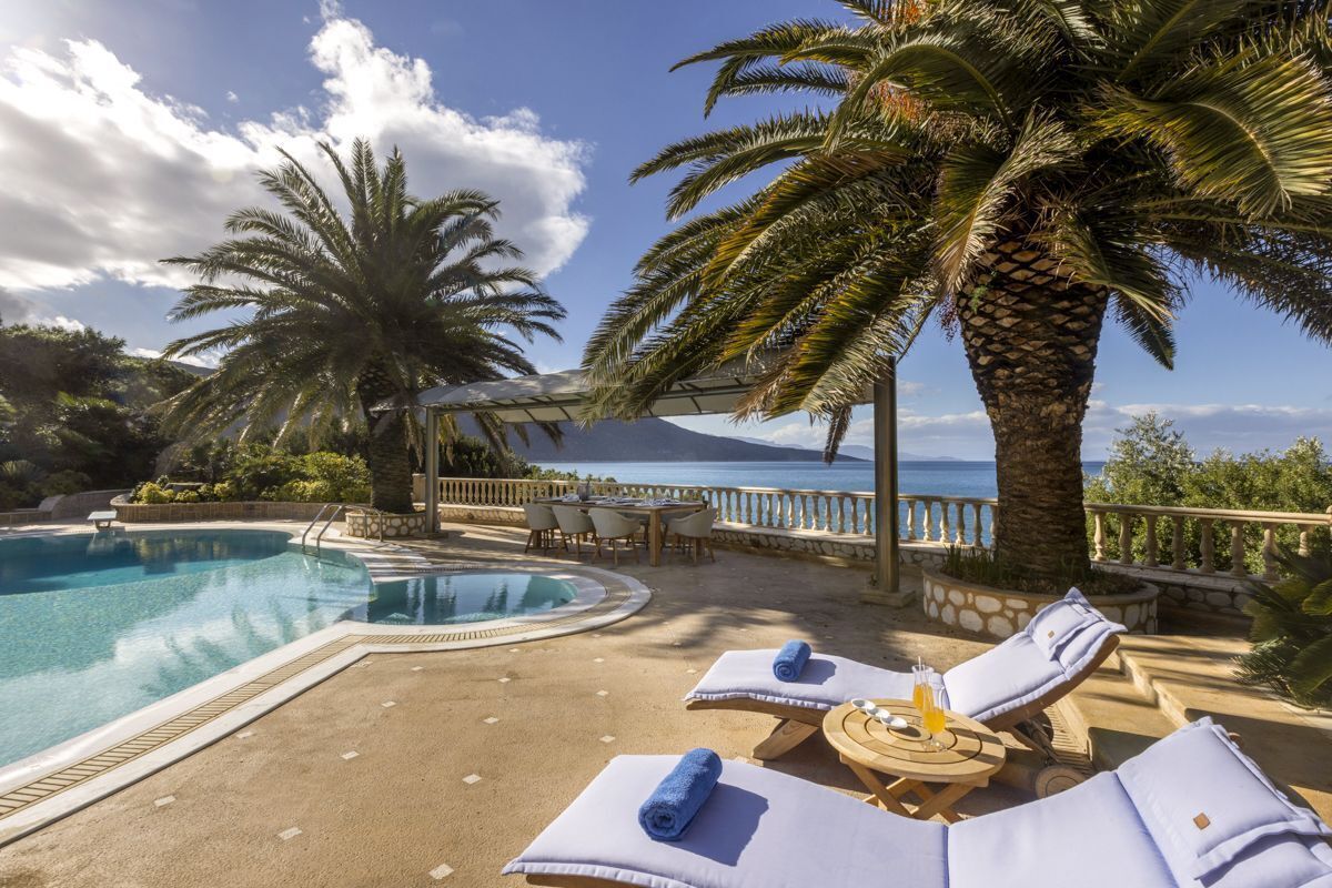 A pool area with lounge chairs and a view of the sea.