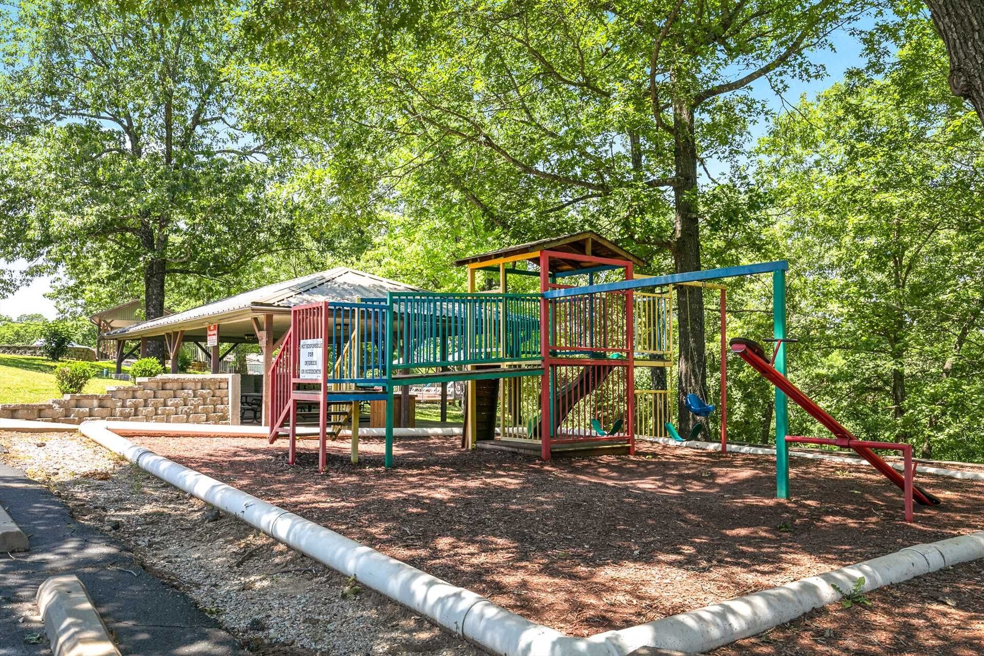 Un parque infantil con una estructura de escalada, un área de descanso techada y suelo de tierra.