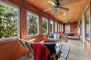 A cabin interior with a dining area, a swing chair, and large windows. - Deluxe Notch Estates Cabin, Close to SDC - 4 BR Suites, 2 Living Areas - 35 (Branson West)