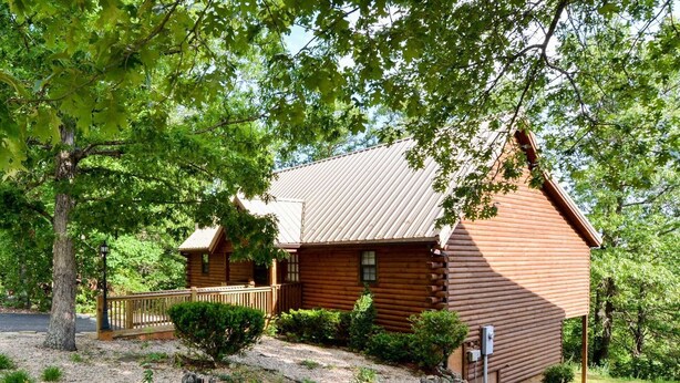 Une cabane en rondins surmontée d’un toit en métal, entourée d’arbres et bordée d’un chemin de gravier.