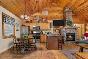 A cozy log cabin interior with a kitchen, dining area, and fireplace.