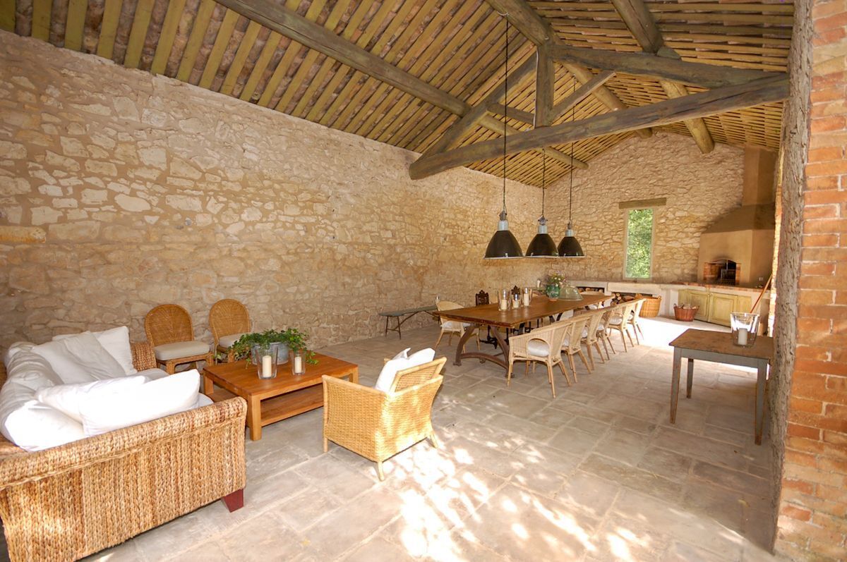Une pièce rustique aux murs de pierre et au plafond en bois, meublée de canapés en osier, d’une table à manger en bois et agrémentée de lampes suspendues.
