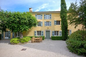 A yellow building with multiple windows and shutters, a gravel courtyard, and a table with chairs. - Maison Cerisaie - Four Bedroom Villa, Sleeps 8 (Pernes-les-Fontaines)