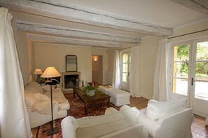 Quarto com mobiliário branco, lareira e vista através de uma porta de vidro.