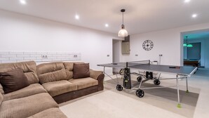 A modern living room with a sofa, a ping pong table, and a clock on the wall.