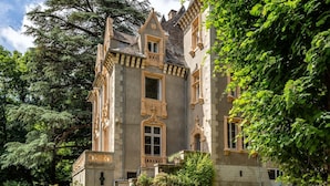 Un edificio histórico con una torre destacada, un balcón y un jardín con asientos.