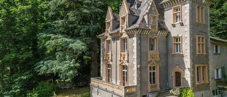 A large, historic building with multiple towers and a well-maintained garden.