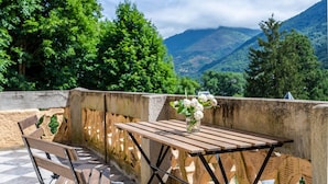 Una mesa de madera con un jarrón de flores, un banco y vistas a montañas y árboles.