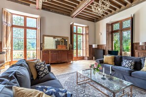 A spacious living room with a large sofa, a glass coffee table, and a view of the outdoors through large windows. - Chateau Des Pyrenees (Bagnères-de-Luchon)