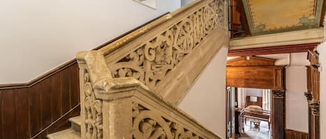 Eine Treppe mit aufwendigen Schnitzereien, die zu einem Raum mit einem Klavier und einem Bett führt.