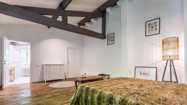 A bedroom with a wooden floor, a bed with a green furry cover, a wooden dresser, a white door, and a framed picture on the wall.