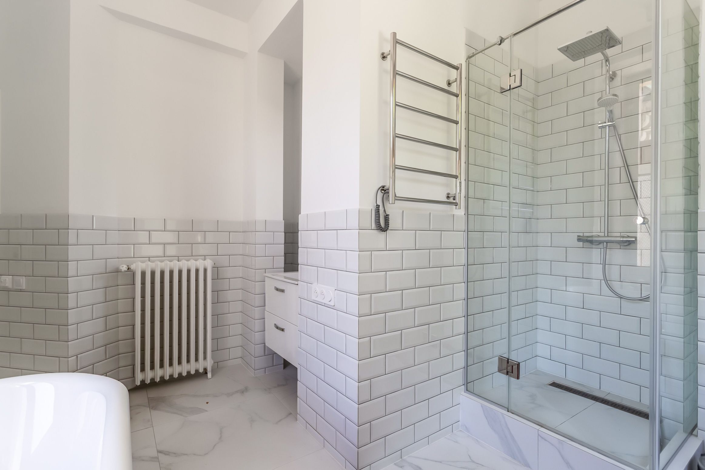 Une salle de bain moderne avec des carreaux de métro blancs, une douche en verre et un radiateur blanc.