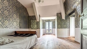 Un dormitorio con una cama grande, piso de madera y papel tapiz estampado.