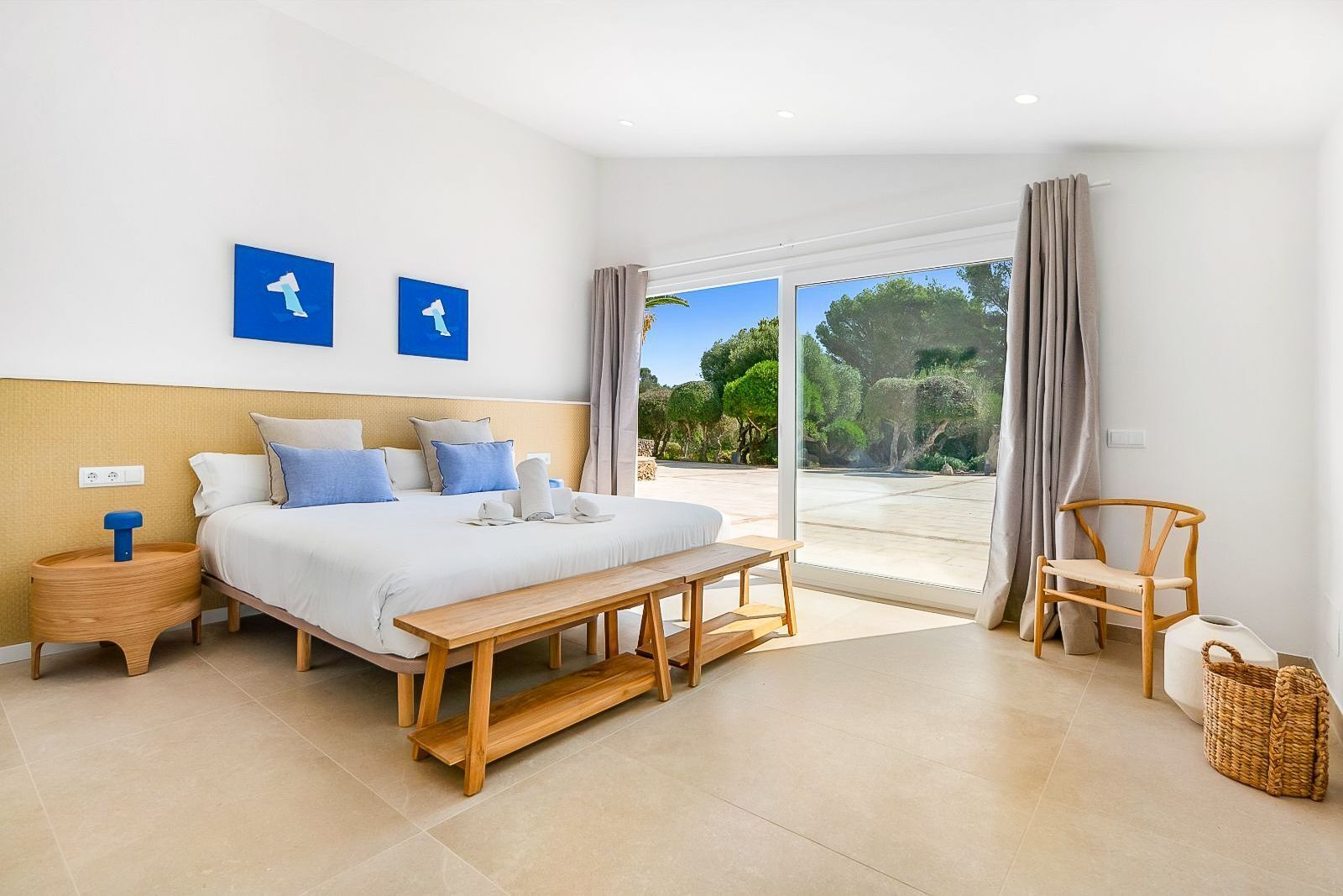 A bedroom with a bed, bedside table, bench, and a view of the outdoors.