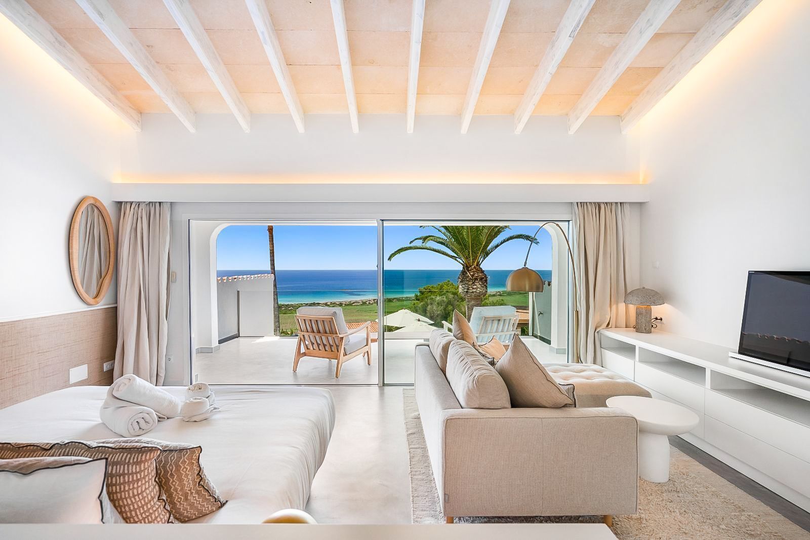 Une chambre d’hôtel moderne dotée d’un grand balcon, d’un canapé, d’une télévision et offrant une vue sur l’océan.