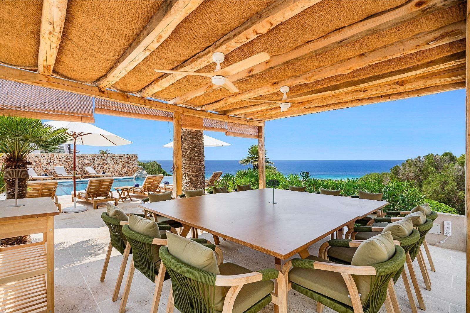 Un patio exterior con mesa y sillas de madera, una piscina y vistas al océano.