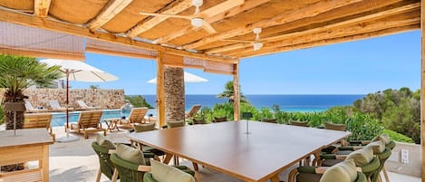 Un patio exterior con mesa y sillas de madera, una piscina y vistas al océano.