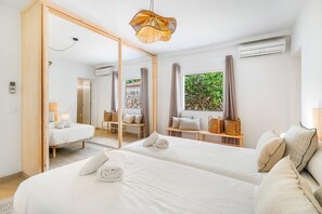 A hotel room with two beds, a large mirror, a window with a view of greenery, and a hanging light fixture. - Villa Cley - Four Bedroom Villa, Sleeps 8 (Alayor)
