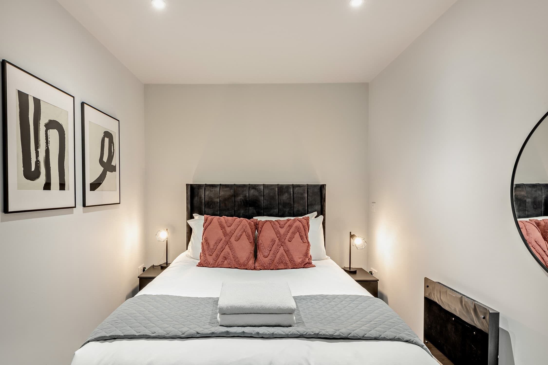 Ein Schlafzimmer mit einem Bett, zwei Nachttischlampen, einem Kopfteil und zwei gerahmten Kunstwerken an der Wand.