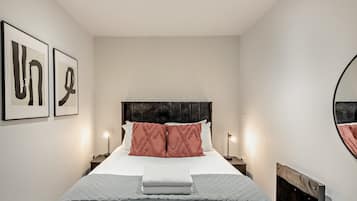 Ein Schlafzimmer mit einem Bett, zwei Nachttischlampen, einem Kopfteil und zwei gerahmten Kunstwerken an der Wand.