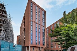 Un edificio moderno de varios pisos con un diseño de esquina destacado, rodeado de otros edificios y andamios de construcción.