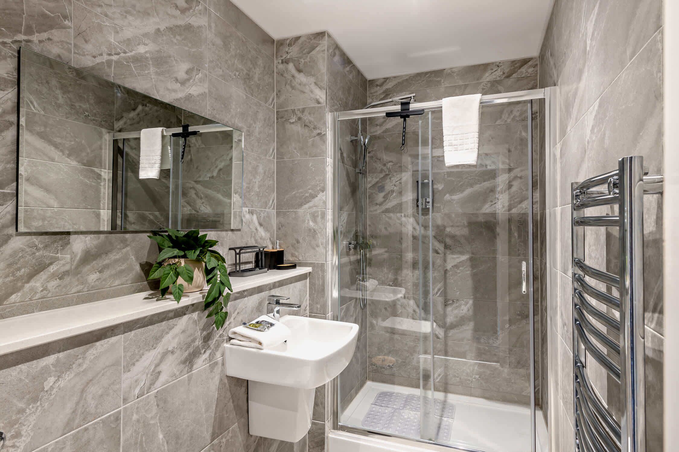 Un baño moderno con ducha envuelta en vidrio, un lavabo blanco y pared revestida de mármol.