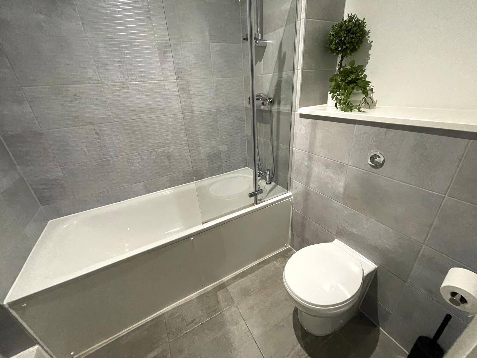 A bathroom with a bathtub, toilet, and a shelf with a plant.