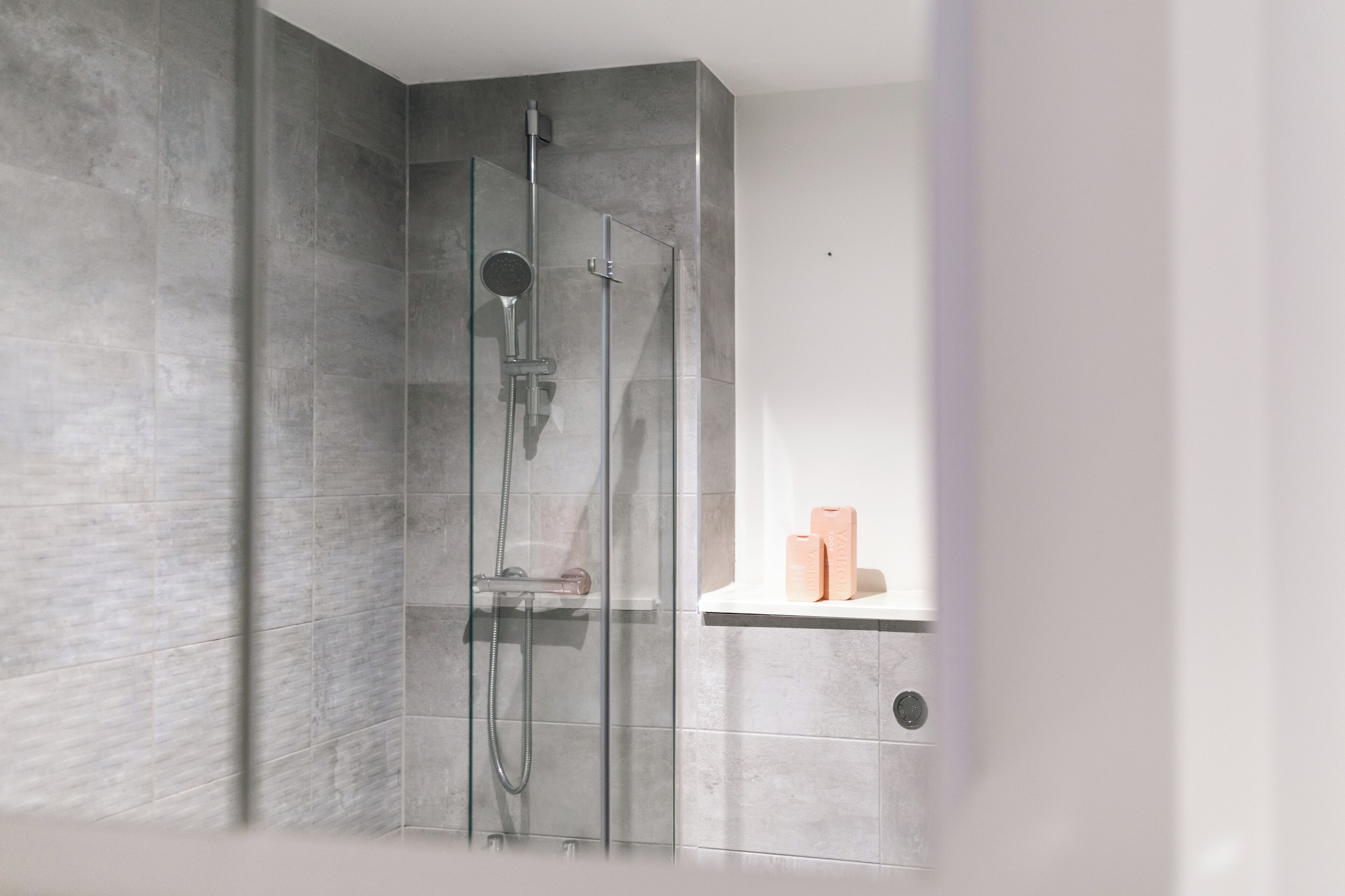 A modern shower with a glass door, a handheld showerhead, and a handheld shower attachment.