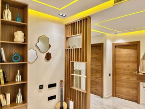 A hallway with a wooden bookshelf, wall-mounted mirrors, a guitar, and a wooden door. - Apartment Guéliz Prestige (Marrakech)