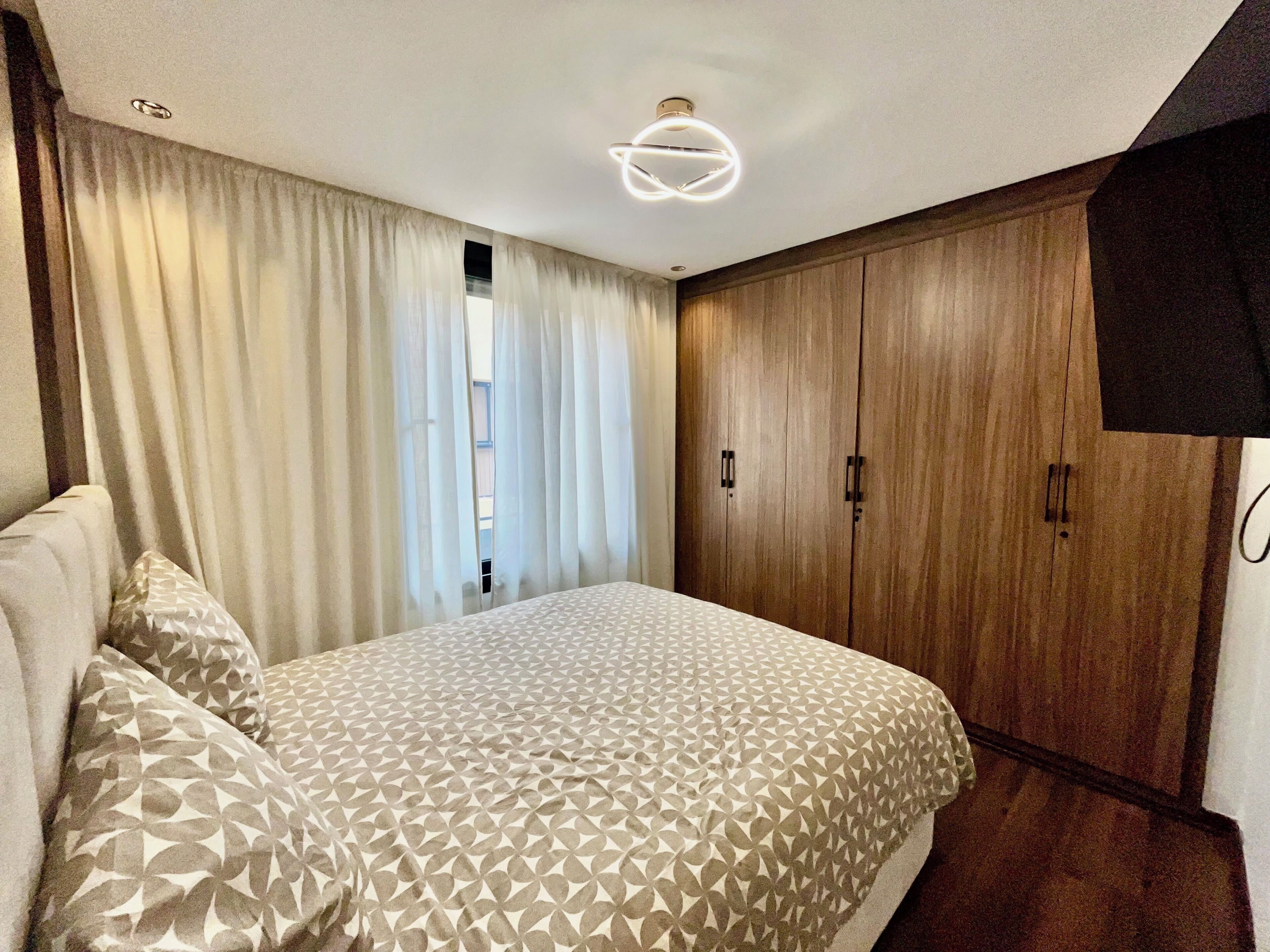 Une chambre à coucher avec un lit, des rideaux, une armoire et un luminaire au plafond.