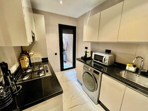A compact kitchen with a stove, microwave, and washing machine. - Apartment Guéliz Prestige (Marrakech)