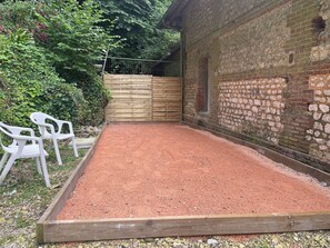 Une zone recouverte de gravier, avec une clôture en bois, un mur de briques et des chaises en plastique blanches.