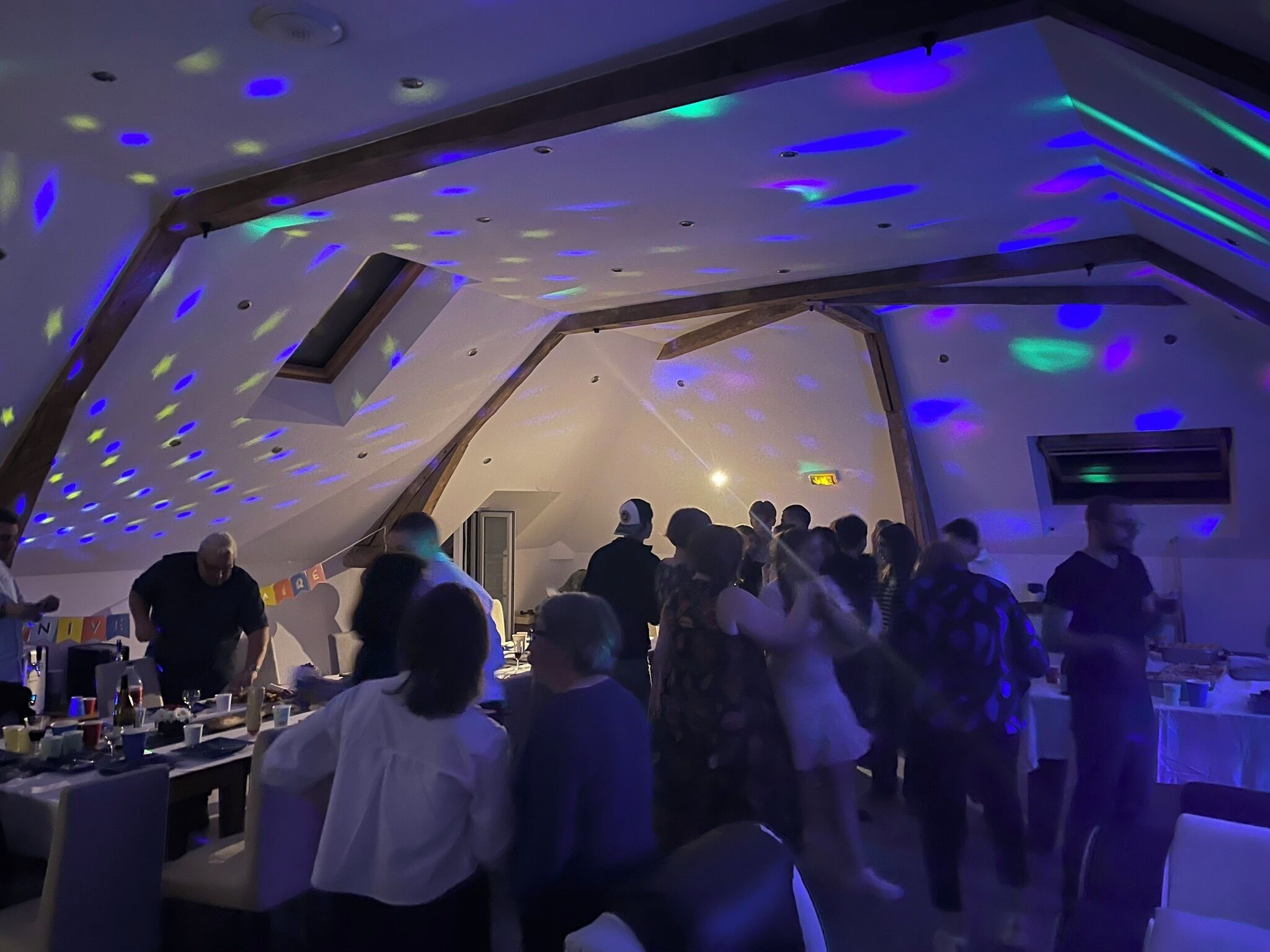 A party in a room with a sloped ceiling and skylights, with people dancing and tables set up.