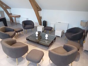 A modern living room with a glass coffee table, multiple armchairs, and a white ottoman.