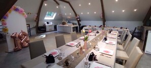 A long dining table set with chairs, balloons, and floral decorations in a spacious room with a sloped ceiling.