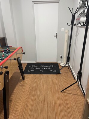 A room with a foosball table, a black mat with text, a door, and a coat rack.