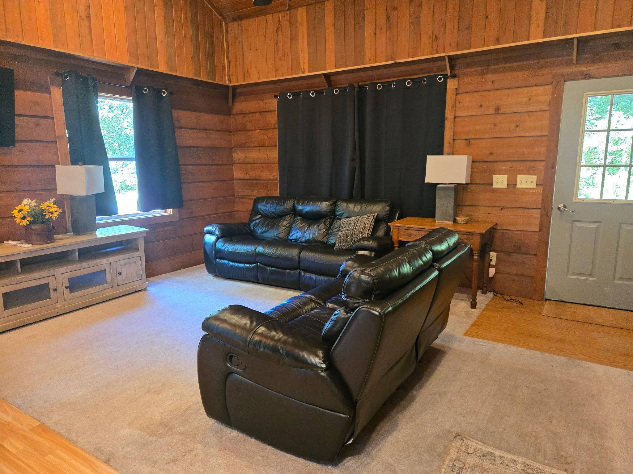 L’intérieur d’une cabane en rondins, avec un canapé en cuir noir, une table en bois et une porte dotée d’une fenêtre.